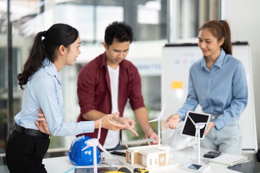 A diverse group of engineers collaborates on a sustainable energy project, showcasing wind turbines and eco-friendly designs in a bright office space.
