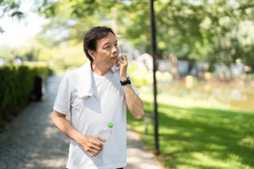 A man wipes sweat from his face and drinks water after exercising in a park, highlighting hydration and wellness.