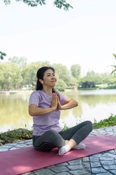 A woman sits in a yoga pose with hands in prayer position, fostering wellness and mindfulness by the lake.