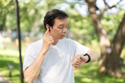 A senior man checks his smartwatch while enjoying music outdoors, emphasizing the blend of wellness and technology in daily life.