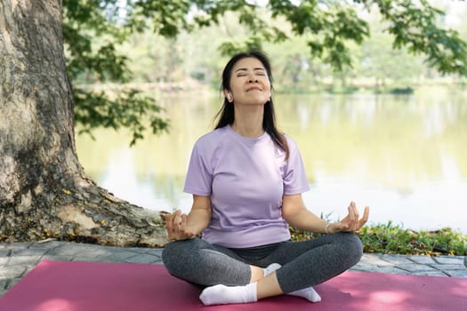 A woman sits cross-legged, meditating peacefully by a lake, embodying wellness and tranquility in nature.