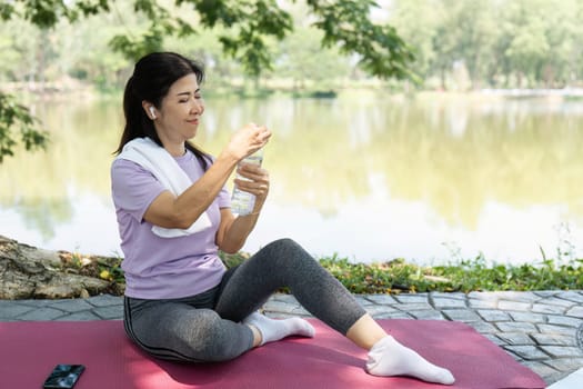 A focused woman sits on a yoga mat, ready to drink water after her outdoor yoga session by the tranquil lake.