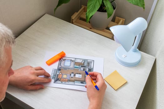 Man studies layout of the small, furnished apartment printed on the sheet of paper placed on the desk