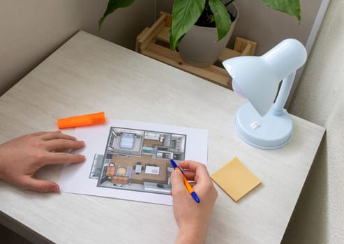 Man studies layout of the small, furnished apartment printed on the sheet of paper placed on the desk