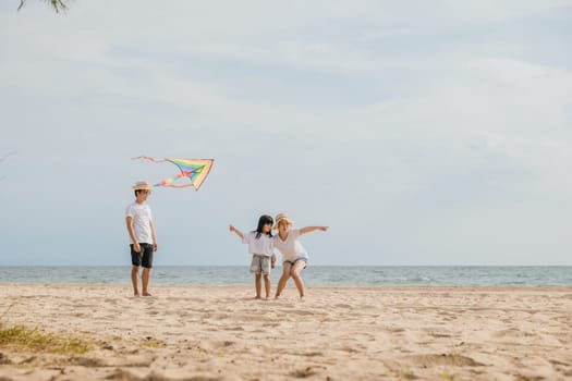 Asian family is flying a kite high in the sky while running on the beach. Happy parents mother and father with their child playing with kite, family is enjoying their time together, summer day