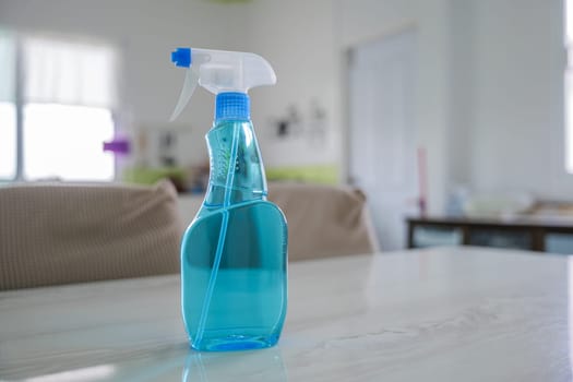 Blue spray bottle with clear liquid on white tabletop, in focus with blurred background. Represents cleaning tools. Glass spray bottle in kitchen setting highlights a modern cleaning concept