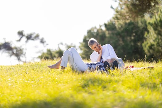 Happy retired couple enjoying a sunny day in nature, lying on a blanket in a meadow