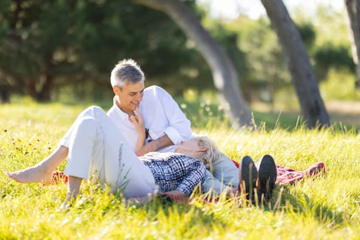 Happy retired couple enjoying a romantic picnic in a park, sharing intimate moments and love in their golden years