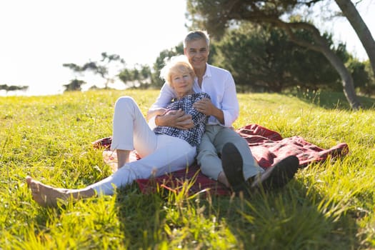 Happy retired couple enjoying a sunny day, embracing on a blanket in a meadow