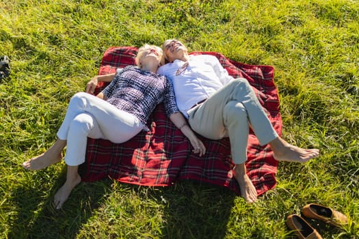 Retired couple lying on a blanket in a meadow, enjoying a relaxing day together