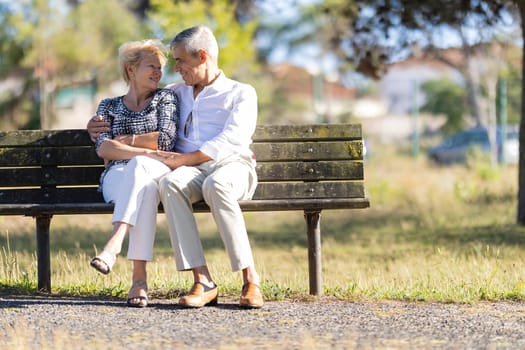 Senior couple enjoying retirement together, sitting on a park bench, embracing and talking on a sunny day