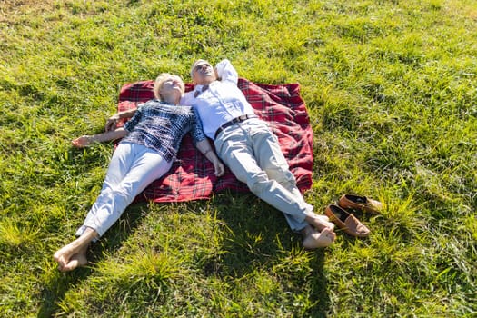Retired couple enjoying a relaxing day lying on a blanket in a peaceful green meadow