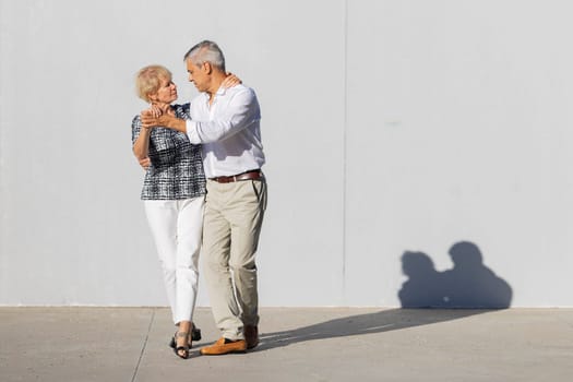 Happy mature couple dancing outdoors in the sun, enjoying retirement and active lifestyle