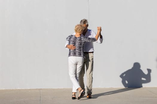 Elderly couple dancing tango in the street in front of a white wall