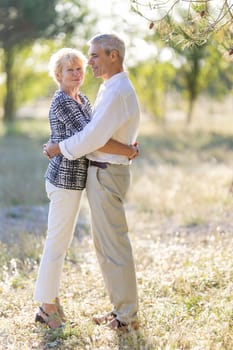 Romantic senior couple enjoying a sunny day in nature, embracing and smiling