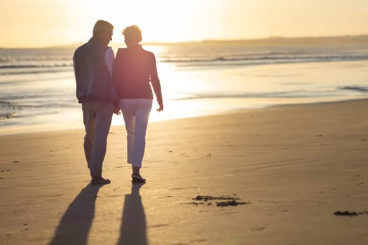 Retired couple enjoying a romantic walk on the beach at sunset