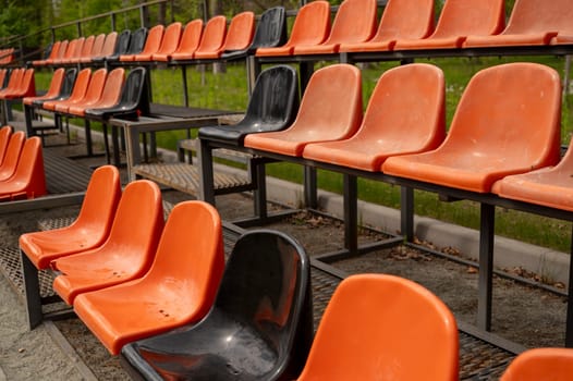 Close up of Rows of empty orange and black plastic seats on grandstand near outdoor sports stadium. High quality photo