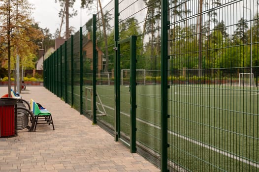 a row of seats for spectators in front of a football pitch. The football pitch is surrounded by a green net.