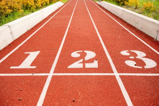 Red running track in stadium, with numbers at the start one, two, three, the running track is deep red. Sport recreation. Helthy lifestyle concept. Running track with lanes over sky and clouds