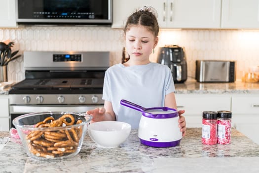 With focused attention, this budding culinary artist dips pretzels into a pot of melted chocolate, creating sweet delights in the warmth of a well-lit home kitchen.