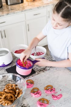 With focused attention, this budding culinary artist dips pretzels into a pot of melted chocolate, creating sweet delights in the warmth of a well-lit home kitchen.