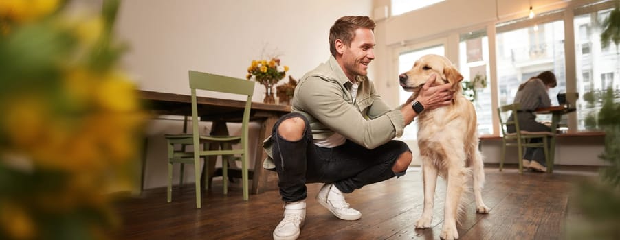 Close up portrait of happy dog owner, man with his pet giving a treat, spending time in animal-friendly cafe or co-working space.