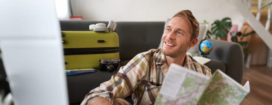 Portrait of handsome smiling guy, tourist going on holiday, holding map, plans where to go on vacation.