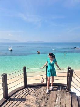 Russian tourist in blue dress enjoying Vietnam beach vacation. Aerial view from pier showing crystal clear water and white sand in Nha Trang.