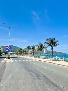 Empty clean road in Nha Trang during siesta time with traffic signs, blue sea featuring traditional Vietnamese boats, palm trees and sunny sky