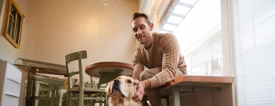 Vertical shot of young smiling man with his dog, golden retriever pet in a cafe.