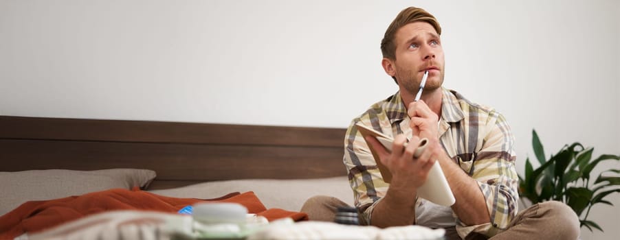 Portrait of thoughtful young man, tourist going on vacation, going through holiday check-list, writing down what he wants to take on travelling.
