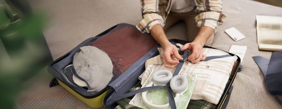 Close up portrait of male hands, man putting clothes inside suitcase, packing for holiday. Tourism and travelling concept