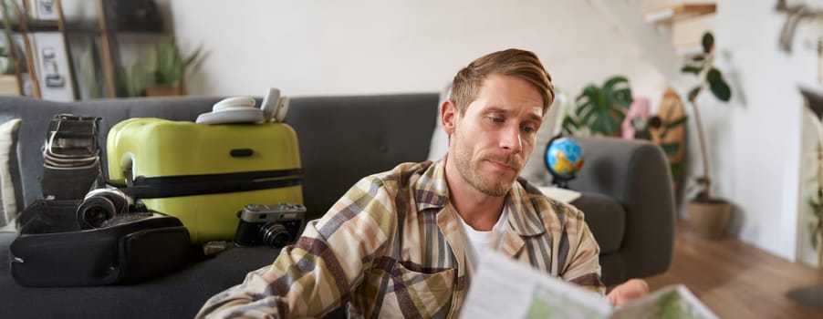 Portrait of man, traveller looks confused at map, studying the route to go on vacation or business trip. Tourism concept