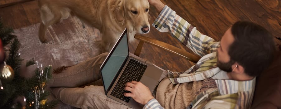 Vertical cropped photo of male hands and body, man petting the dog while working on laptop in cafe, drinking coffee.