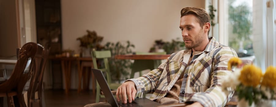 Lifestyle and workplace concept. Young handsome man in casual clothes, sitting in cafe with laptop, studying online, working remotely from coffee shop.