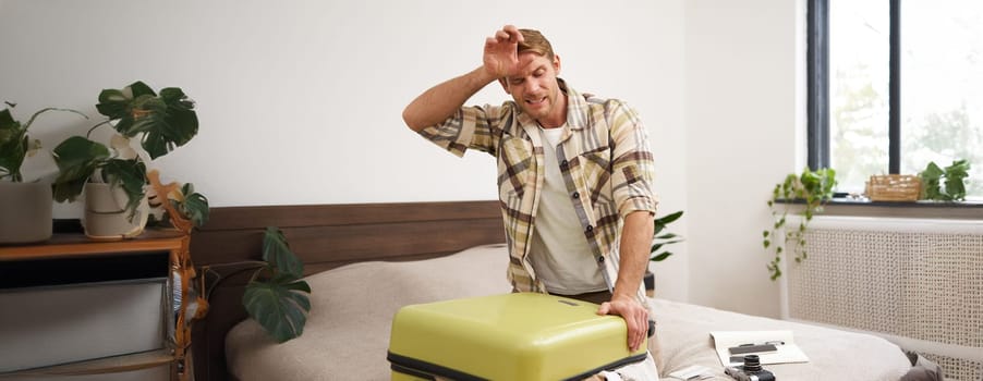 Portrait of man struggling to close suitcase full of clothes, putting effort to pack luggage for holiday, going on long vacation. Tourism and travel agency concept