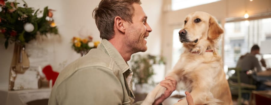Close up portrait of cute dog and happy man, guy hugging his pet, spending time in animal-friendly cafe, waiting for an order.