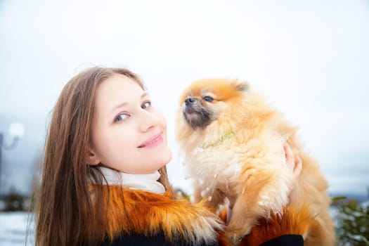A woman lovingly carries her fluffy Pomeranian dog during a winter outing in the snow.