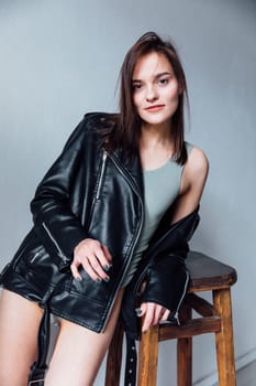 Portrait of a beautiful fashionable brunette woman in a leather jacket on a gray background