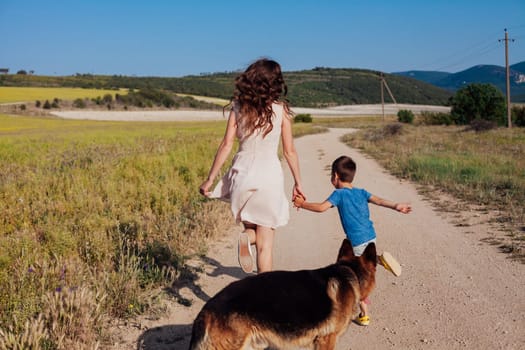 Mother with little son and dog walking in rural field in summer by road