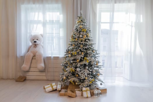 Christmas tree with gifts and toys in the interior of a room with a window