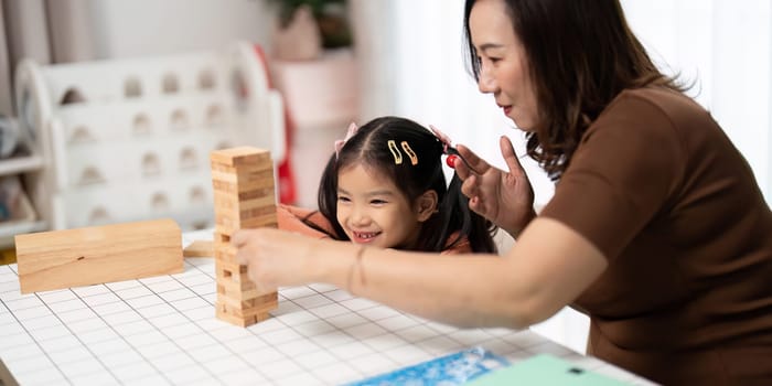 A mother and her daughter laugh and play together while stacking Jenga blocks, fostering a joyful family atmosphere.