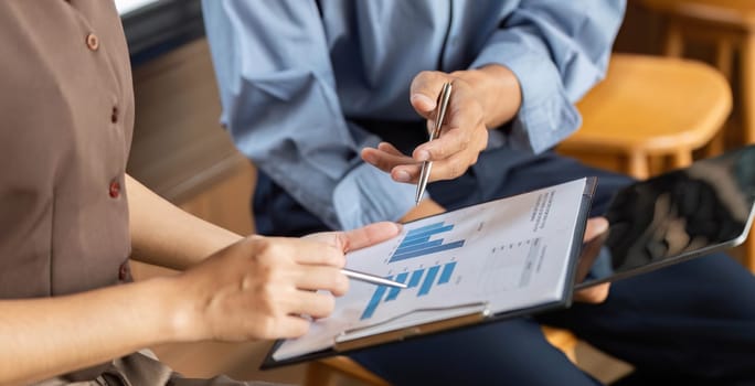 Two business professionals engage in a collaborative discussion, analyzing financial data and charts on a tablet in a contemporary office setting.