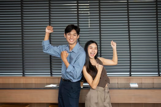 Two professionals celebrating their achievements with joyful poses in a contemporary workspace.