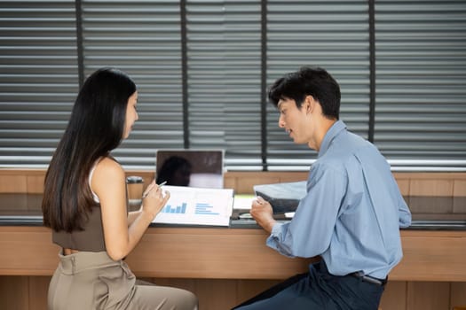 A young businesswoman and businessman analyze data together, demonstrating collaboration and strategic planning in a contemporary workspace.
