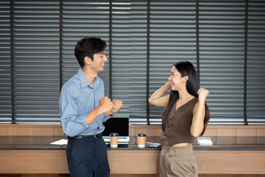 Two young professionals joyfully celebrating their achievements together in a modern office setting.