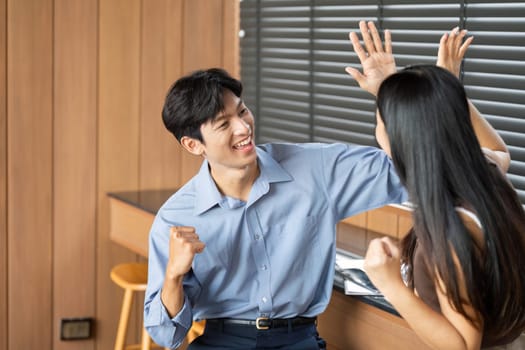 A young man and woman celebrating their success with high-fives in a modern workspace, representing teamwork and motivation.