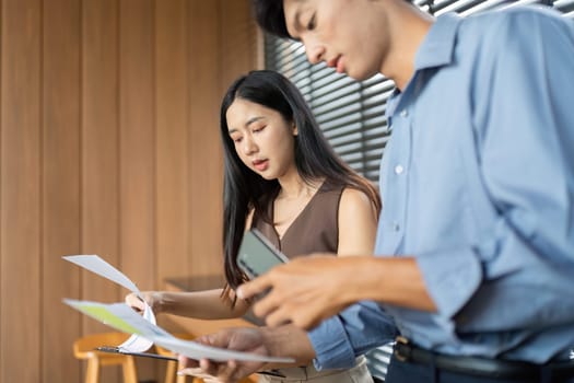 A businesswoman and businessman are reviewing documents and discussing project details in a stylish, modern office environment.