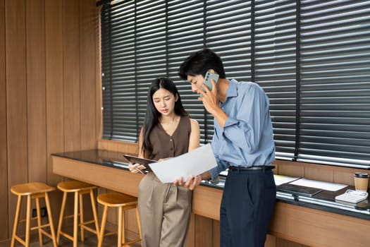 A businesswoman and businessman analyze project documents together, showcasing teamwork and collaboration in a modern workspace.