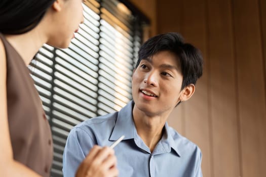A young businessman engages in a conversation with a businesswoman, exchanging ideas and insights in a contemporary office environment.